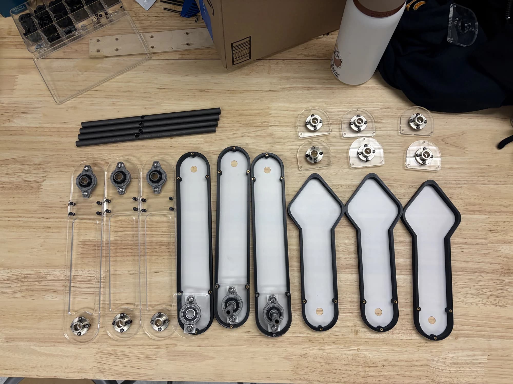 Pendulum arms, shafts, bearings, hubs, and illuminated panels organized before assembly