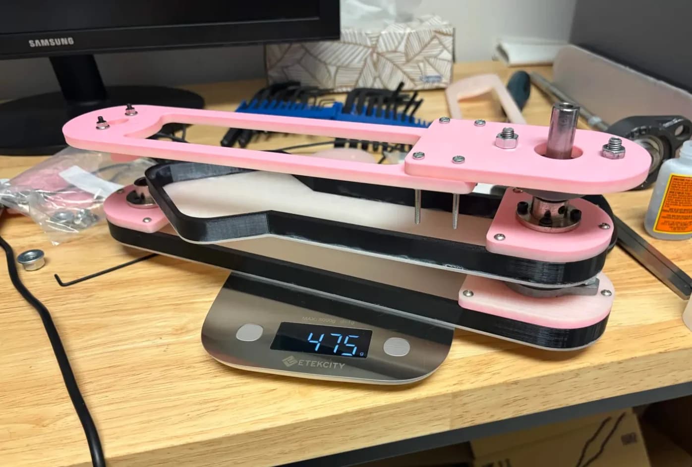 Pink and black pendulum prototype with shafts and fasteners assembled on a workbench scale